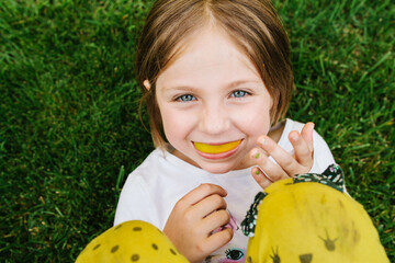 Portrait of a girl laying in the grass with an orange slice in her mouth