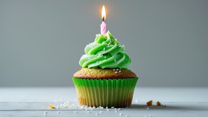 Green cupcake with sprinkles and a lit birthday candle set against a background.