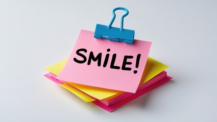 Smile written on a pink sticky note placed on a white surface.