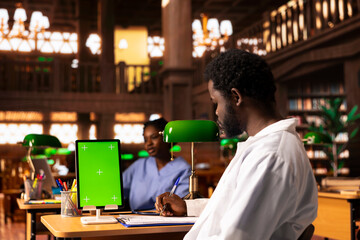 Black medical student reviewing case files in the library next to chroma key screen, preparing for a lecture or study session on medical practices. Med school pupil learns for a career.