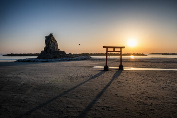 日の出を迎える海岸の鳥居と印象的な岩
