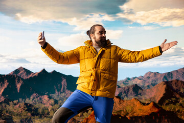 Male content creator recording a video surrounded by mountain peaks in the clouds, climbing a...
