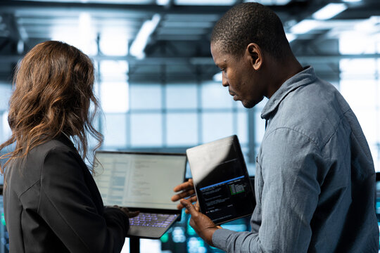 System administrators in data center using laptop and tablet, integrating green technologies. IT specialists in server room using devices to implement sustainable energy solutions