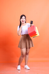 Excited woman with shopping bags and phone on orange background.