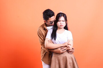 Fototapeta premium a adult couple indonesia hugging annoyed expression where the man stands and the woman faces the camera romantically. isolated on orange background