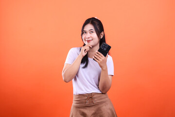 Obraz premium Woman in white shirt holding a mobile phone on orange background smiles at camera