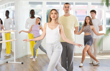 Fototapeta premium Beautiful young woman and man with multinational group training twist or charleston dance movements at modern dance salon