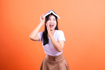 Woman holding open book on her head laughing looks to her right isolated on orange background