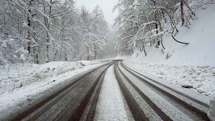 A winding road covered in snow, surrounded by frost-laden trees in a winter landscape