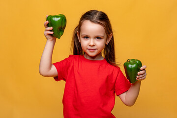 Cute little girl in a red t-shirt on a yellow background, holding two green peppers and smiling. The child loves eco vegetables, concept of healthy child nutrition. Space for text, organic food © Irina Mikhailichenko