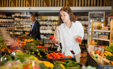 Young girl with a grocery cart carefully selects fresh vegetables, standing near the counter in the supermarket