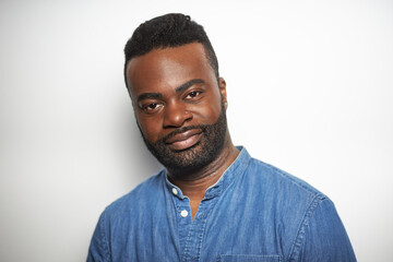 Portrait of a confident Black man with well-groomed beard wearing a denim shirt against a white background
