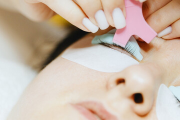 Girl cosmetologist laminates and paints woman eyelashes