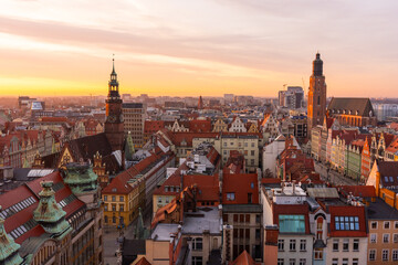 Obraz premium Scenic aerial view of historic European city at sunset with colorful rooftops, old town architecture, and church towers. Warm golden light enhances the charm of the picturesque urban landscape.