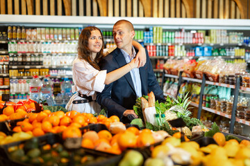 Happy couple is standing with trolley with food for dinner in a supermarket