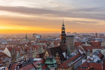 Naklejka premium Aerial view of Wroclaw, Poland, at sunset, showcasing stunning blend of medieval and modern architecture with red rooftops, historic churches, and contemporary buildings glowing in golden light.