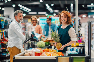 Smiling cashier holding pineapple at checkout in supermarket