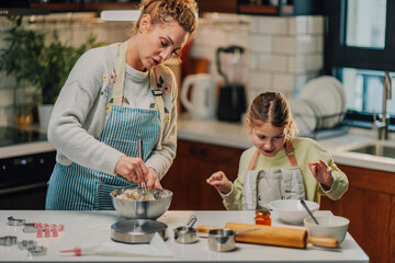 Mother and daughter baking cookies, mixing ingredients in kitchen