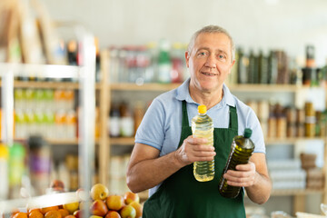 Polite mature male seller kindly offering bottled vegetable oil in grocery store
