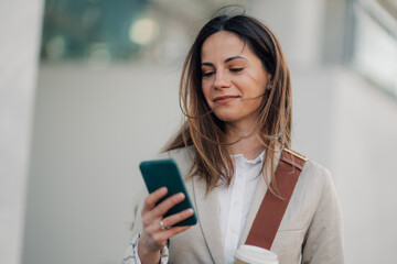 Businesswoman using smartphone and holding coffee outside office building