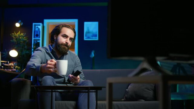 Man appalled by upsetting breaking news story on TV, doing phone call to family member. Person at home scared by troubling events broadcasted on TV, calling friend using smartphone, camera B
