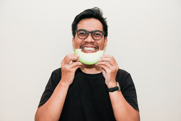 A Southeast Asian Funny face Man holding melon and eating melon on cream isolated background. Man...
