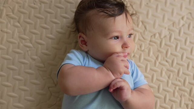 Baby lying on soft mat, sucking hand, self-soothing behavior, early development, comforting reflex, relaxed expression, feeling secure, peaceful moment in a nurturing environment