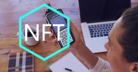 Person scanning QR code on smartphone with NFT text animation over desk - Powered by Adobe