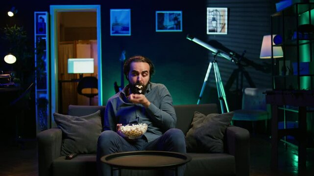 Man in apartment chocking on food while watching movie on TV and eating popcorn. Person getting throat clogged while swallowing snack, doing heimlich maneuver on couch, fighting for his life, camera B