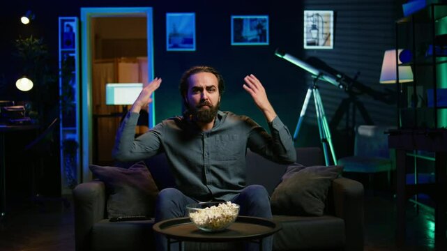 Supporter watching sports match on live broadcast, raging on couch in anger seeing team mistake. Angry man looking at football competition fuming, releasing pent up emotions, camera B