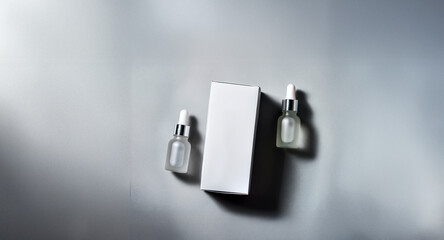 Minimalist product shot featuring two dropper bottles with silver caps and a white box on a soft grey surface with subtle shadows.