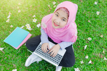 Asian Islamic children do homework with laptop on green grass, Muslim children connect internet and search information, she feeling fun and smile, education time in the garden.
