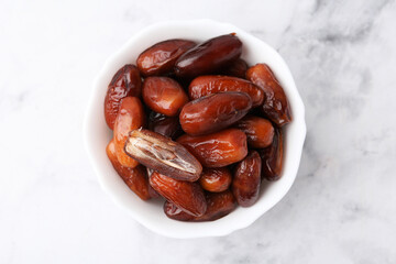Tasty dried dates in bowl on white marble table, top view