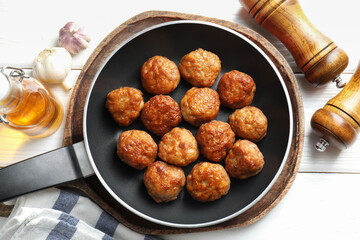 Tasty meatballs in frying pan and ingredients on white wooden table, flat lay