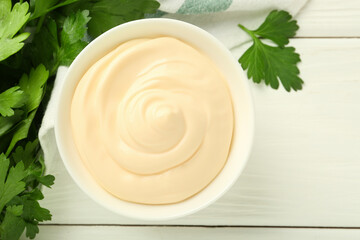 Delicious mayonnaise sauce in bowl and parsley on white wooden table, top view