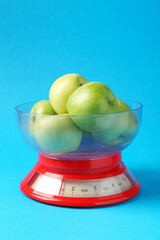 Kitchen scale with apples on light blue background