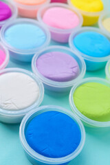 Different colorful modeling clay in plastic jars on light blue background, closeup