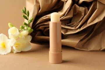 Lip balm and freesia flowers on light brown background, closeup
