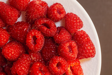 Close-up image of juicy raspberries with water droplets, arranged on a white plate against a dark...