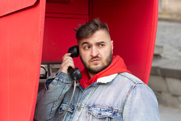 Horizontal photo. Young adult fat white man in blue jeans denim jacket, red hoodie calls from...