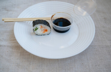 sushi roll with chopsticks and wasabi sauce in a plastic container on a white plate.