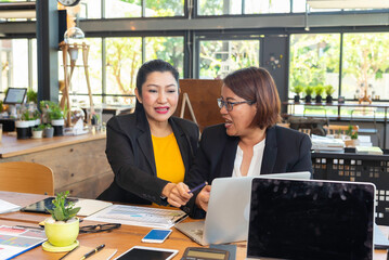 Two happy busy female employees working together using computer planning project.