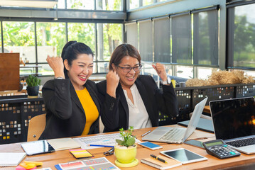 Two happy busy female employees working together using computer planning project.
