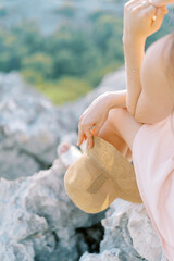 Young woman with a hat in her hand sits on a rock, resting her chin on her hand. Cropped