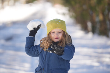 Child playing in Snowball fight. Kid boy Snowball fight in the snow. Happy kid in warm clothes enjoying snow falling and Snowball fighting. Child play with snow outdoors during first snowfall.