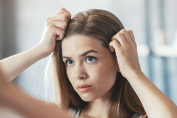Fototapeta premium Millennial woman with problematic hair looking in mirror at bathroom, copy space