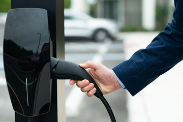 Male hand with Electric car charging. Eco vehicle. Recharging battery for electric car. EV Electric...