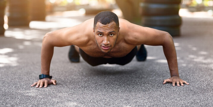Strong black guy doing push ups or plank exercise after running at park in morning, panorama