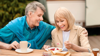 Happy senior couple having toasts with jam and coffee for breakfast at campsite