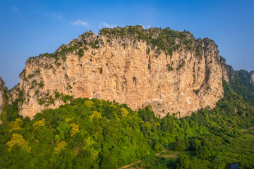 This rocky mountain is called Khao E-Bid, located in Phetchaburi Province, Thailand. It appears orange as it is illuminated by the setting sun.